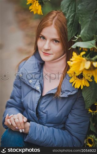 A large portrait of a red-haired girl against the background of nature.. A girl on the background of sunflowers in autumn 2753.