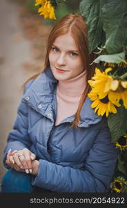 A large portrait of a red-haired girl against the background of nature.. A girl on the background of sunflowers in autumn 2753.