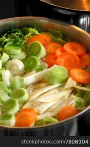 A large pot of vegetable soup boiling on top of a stove. Focus is across the middle of image.