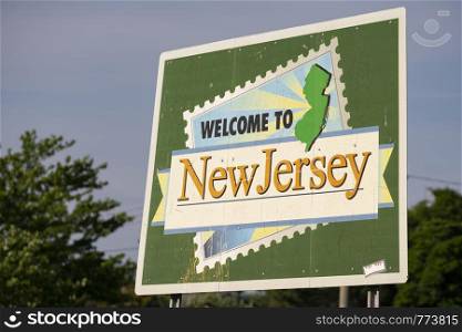 A large roadside metal banner welcomes travelers to the state of New Jersey