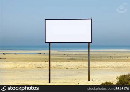 A large sign on an idyllic beach with no text and a small bird - a Southern Grey Shrike - perched on one corner.