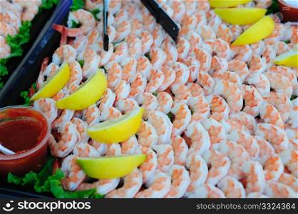 A large tray of shelled and cooked shrimp with lemon slices and seafood sauce.. Cooked Shrimp And Lemon Wedges