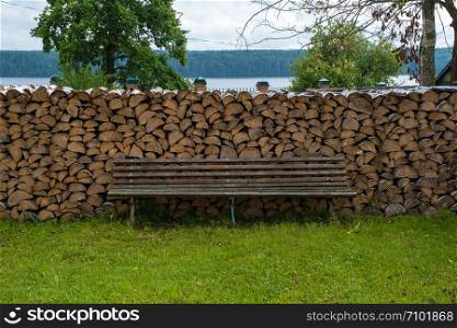 A large woodpile of birch wood and a wooden bench for relaxing on a summer day.