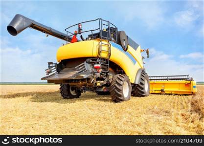 A large yellow harvester harvests wheat from a field on a clear fall day against a blue sky and a flat horizon. Close-up, copy space.. A large yellow agricultural harvester harvesting crops against the backdrop of a wheat field on a clear autumn day.