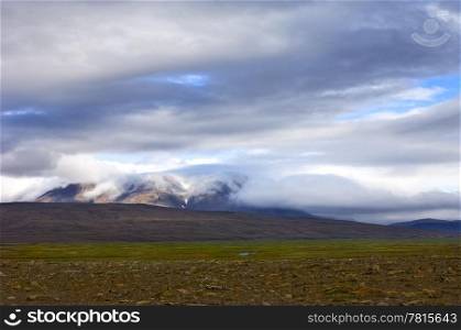 A layered Icelandic tundra landscape, with clouds rolling in from the glacier in the background