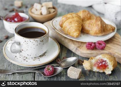 A light breakfast consisting of a cup of black coffee and croissants with a stuffing from raspberry jam