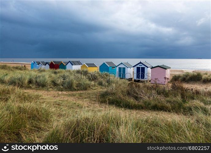 A line of beach huts next to the sand dunes, in a variety of colours, at Southwold, Suffolk