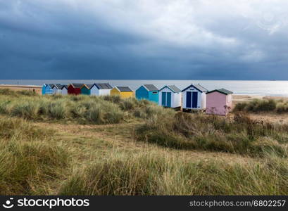 A line of beach huts next to the sand dunes, in a variety of colours, at Southwold, Suffolk