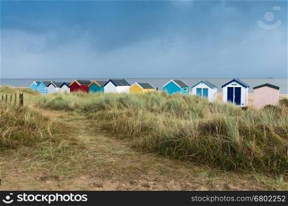A line of colourful beach huts next to the sand dunes at Southwold, Suffolk