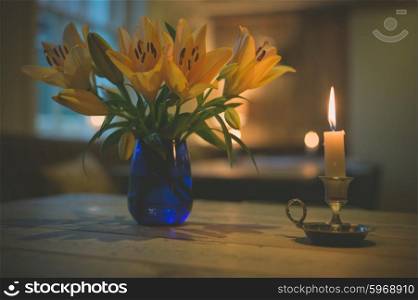 A lit candle and a vase with blooming lillies on a table in a dining room