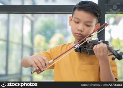 A Litt≤Asian kid playing and practice violinμsical string instrument against in home, Concept of Musical education, Insπration, Teena≥r art school student.