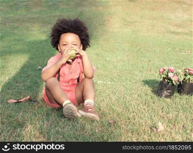 A little African boy wearing pink shirt is playing and eating apple in backyard