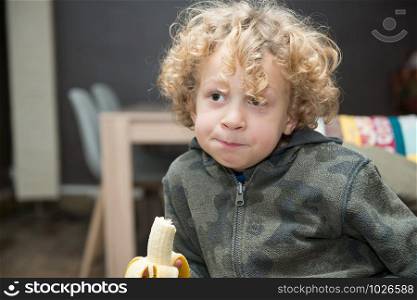 a little blond boy eating a banana
