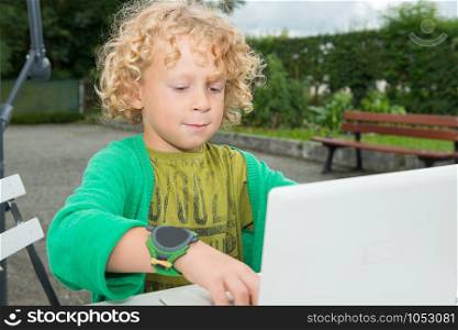 a little blond boy using a laptop, outdoors