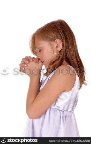 A little blond girl standing in profile with her hands folded and praying,isolated for white background.