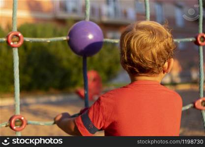 A little boy climbing through a net of a children's playground at sunset