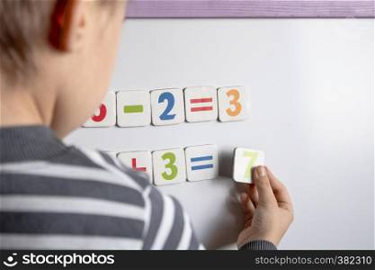 A little boy solves a difficult task. Against the background of the school board with numbers in their hands and counts examples.. A little boy solves a difficult task. Against the background of the school board with numbers in their hands.