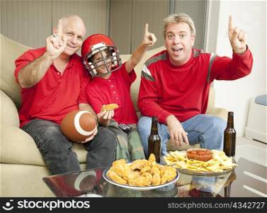 A little boy watching the super bowl with his father and uncle.