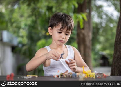 A little boy wearing a comfortable tank top playing with some toy animal figurines on the table at home.Social distancing concept.
