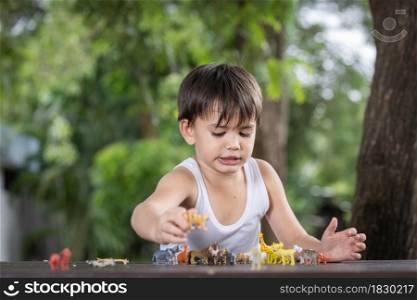 A little boy wearing a comfortable tank top playing with some toy animal figurines on the table at home.Social distancing concept.