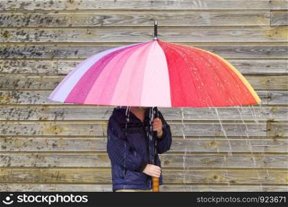 a little boy with red hair hides from the rain in late summer, a multi-colored umbrella in the hands of a child. a little boy with red hair