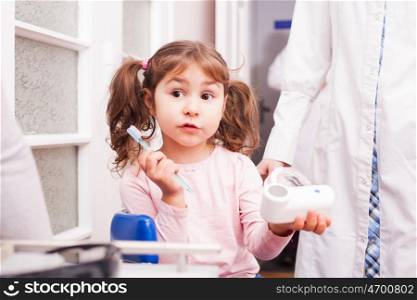 A little girl holds a transparent dentures and toothbrush in hand in the dental office. The girl in dental office