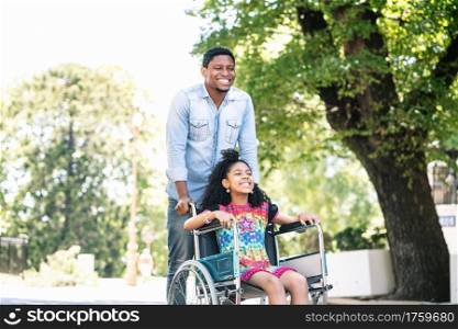 A little girl in a wheelchair enjoying and having fun with her father while on a walk together outdoors.