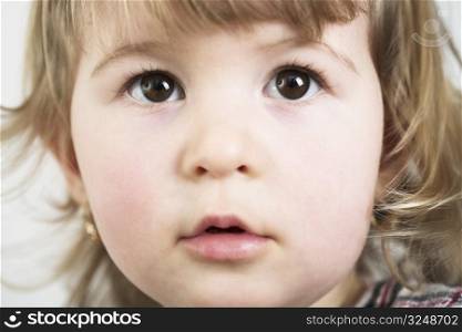 A little girl looks at the camera with big wondering eyes.