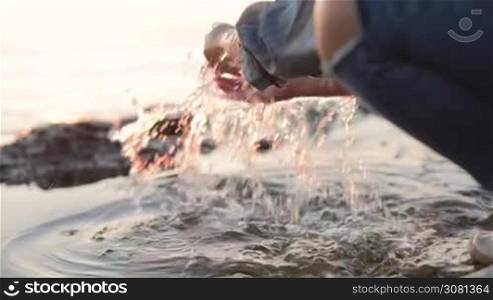 A little girl splashing sea water by the sea coast. Close-up. Sunset at the sea. Slow motion