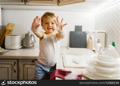 A little girl wipes the dishes on the kitchen. Baby doing housework at home. Young housewife clean the house. Little girl wipes the dishes on the kitchen