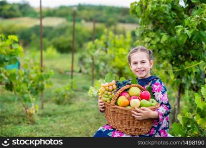 A little girl with a basket, with red apples and grapes in the garden.. A little girl with a basket, with red apples and grapes .