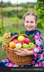 A little girl with a basket, with red apples and grapes in the garden.. A little girl with a basket, with red apples and grapes .