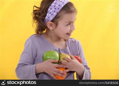 A little girl with her arms full of fruits.