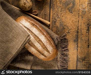 a loaf of bread on a cloth napkin on a wooden surface, top view. loaf of bread top view