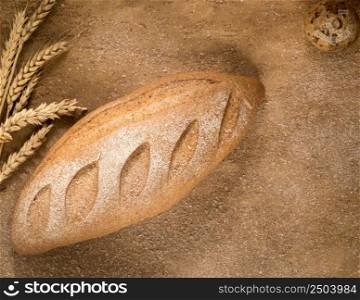 a loaf of bread with an ear of wheat and crumbs on the plastered surface, top view. loaf of bread top view