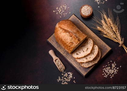 A loaf of brown bread with grains of cereals on a wooden cutting board on a dark concrete background. A loaf of brown bread with grains of cereals on a wooden cutting board