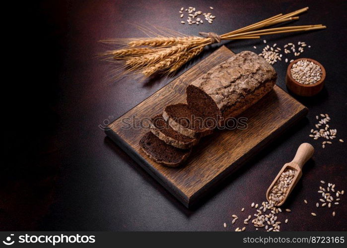 A loaf of brown bread with grains of cereals on a wooden cutting board on a dark concrete background. A loaf of brown bread with grains of cereals on a wooden cutting board