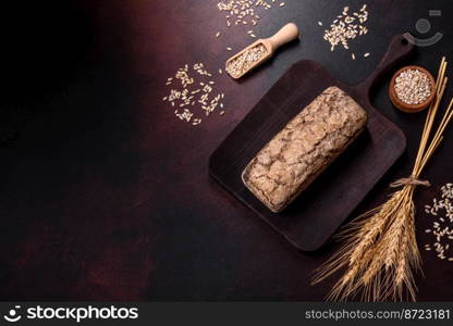 A loaf of brown bread with grains of cereals on a wooden cutting board on a dark concrete background. A loaf of brown bread with grains of cereals on a wooden cutting board