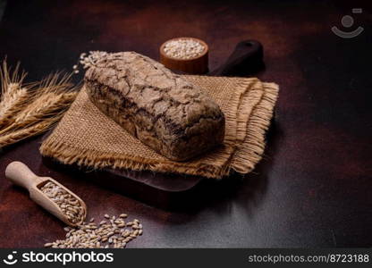 A loaf of brown bread with grains of cereals on a wooden cutting board on a dark concrete background. A loaf of brown bread with grains of cereals on a wooden cutting board