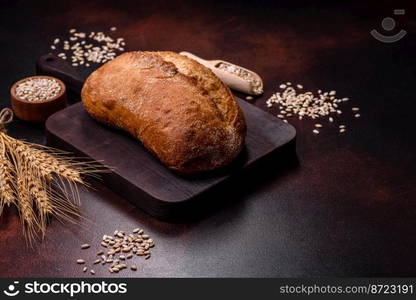 A loaf of brown bread with grains of cereals on a wooden cutting board on a dark concrete background. A loaf of brown bread with grains of cereals on a wooden cutting board