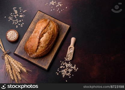 A loaf of brown bread with grains of cereals on a wooden cutting board on a dark concrete background. A loaf of brown bread with grains of cereals on a wooden cutting board