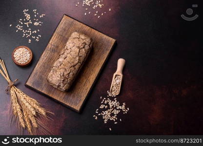 A loaf of brown bread with grains of cereals on a wooden cutting board on a dark concrete background. A loaf of brown bread with grains of cereals on a wooden cutting board