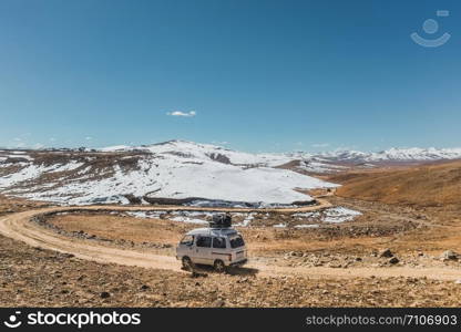 A local bus with luggage on the roof running along the unpaved road with landscape view of snow capped mountains at Deosai plain national park in Astore. Gilgit Baltistan, Pakistan.