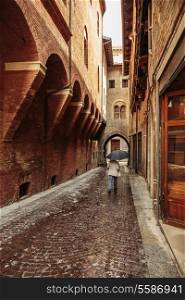 A lone passerby with an umbrella on a narrow street in the old city of Bologna Italy