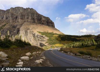 A lone white car makes a curve under the tall peaks of the Rocky Mountains
