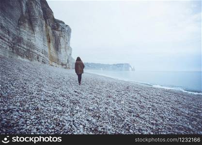 a lonely girl walks along the ocean in the Etretat. France