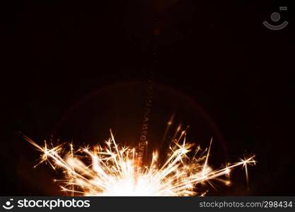 A long exposure close-up shot of a sparkler with flying sparks at night.