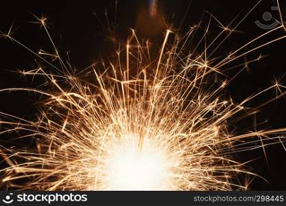 A long exposure close-up shot of bright sparks flying from a sparkler at night.