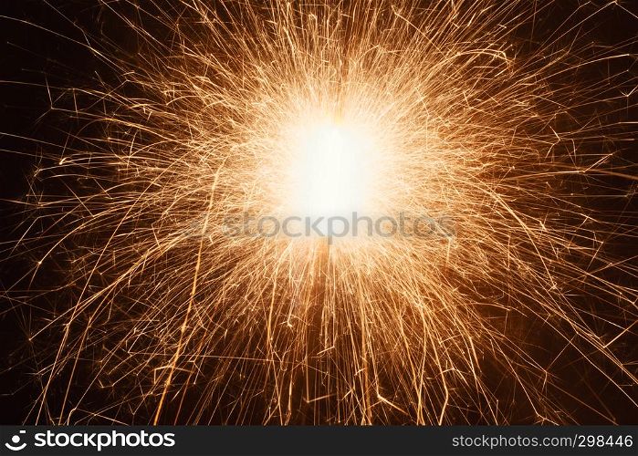 A long exposure close-up shot of bright sparks flying from a sparkler at night.