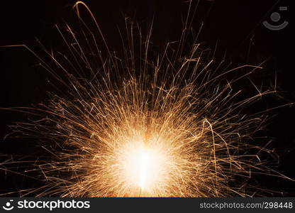 A long exposure close-up shot of bright sparks flying from a sparkler at night.